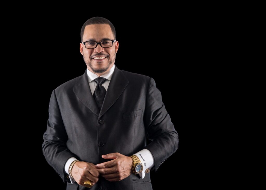 Bishop Tiangello T. Hill in black and white suit and tie.